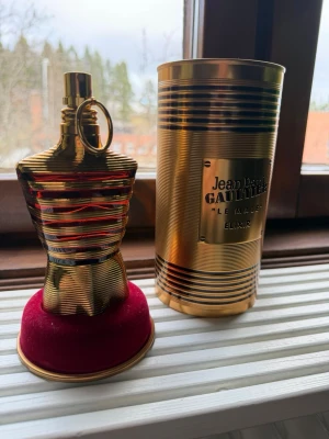 Jean Paul Gaultier Le Male Elixir - Säljer en Jean Paul Gaultier Le Male Elixir parfym i en unik guldfärgad flaska formad som en manlig torso. Flaskan har eleganta ränder och kommer med en matchande guldfärgad metalltub med märkets logga. Perfekt för dig som gillar lyxig och iögonfallande design.