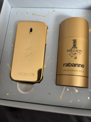 Paco Rabanne 1 Million presentbox - Lyxig presentbox från Paco Rabanne med 1 Million parfym och deodorant stick. Båda produkterna har en snygg guldfärgad design och levereras i en elegant grå ask med guldmönster och stjärndetaljer. Perfekt för dig som gillar exklusiva dofter och stilren förpackning.