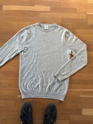 Grå cashmere-tröja John Henric - Mjuk och stilren grå stickad tröja från John Henric i 100% cashmere. Tröjan har rund halsringning, långa ärmar och ribbade muddar vid ärmslut och nederkant. Perfekt för dig som gillar klassisk och enkel stil.