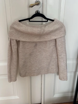 Beige off shoulder stickad tröja - Säljer en beige stickad tröja med bred off shoulder-krage och långa ärmar. Tröjan har ribbstickade detaljer vid krage, ärmslut och nederkant. Perfekt för dig som vill ha en mysig och trendig look.