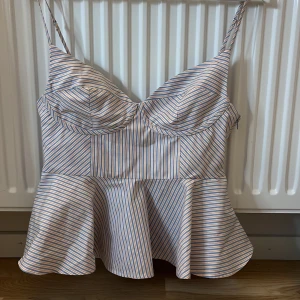 Randig peplum korsettopp från Zara - Superfin korsettinspirerad topp från Zara med peplumvolang. Topp i vitt tyg med smala blå och orange ränder, justerbara smala axelband och markerade kupor. Perfekt för dig som vill ha en feminin och trendig look. Helt oanvänd utan prislapp. M men passar S