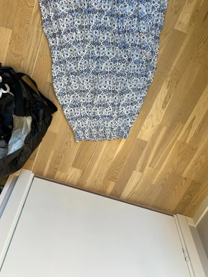 Blommig långkjol från 157, XS - Säljer en långkjol från 157 i storlek XS. Kjolen är vit med blått blommönster och har en smockad midja för skön passform. Perfekt för dig som gillar en romantisk och somrig stil.
