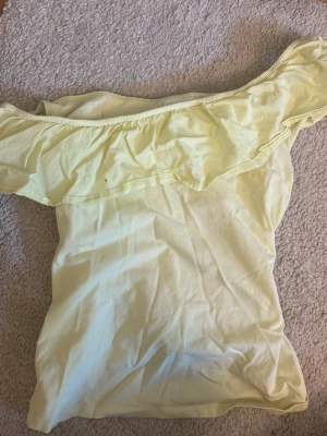 Off shoulder topp - Snygg ljusgul offshoulder topp med volangdetalj längs axlarna. Perfekt för varma dagar och ger en fräsch look. Tillverkad i mjukt bomullsmaterial som känns skönt mot huden.