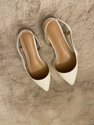 Vita slingback pumps med spetsig tå - Snygga vita pumps med spetsig tå och öppen häl i slingback-modell  och en stilren design som passar till många olika outfits. Tillverkade i ett slätt material med beige innersula för extra komfort. 