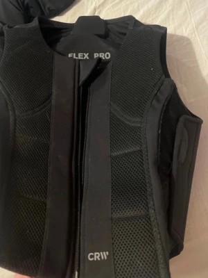 Svart FLEX PRO träningsväst - Säljer en svart skyddsväst från FLEX PRO CRW, perfekt för ridning eller andra sporter där extra skydd behövs. Västen har meshpaneler för ventilation, dragkedja framtill och justerbara kardborreband i sidorna för bästa passform. köpt för över 1100kr helt ny så säljer inte för under 550kr