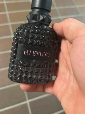 Valentino svart parfymflaska tom - Säljer en parfym från Valentino i en cool svart flaska med nitar och struktur. Flaskan har en modern design med rosa text på etiketten och känns riktigt lyxig. Perfekt för dig som gillar exklusiva dofter och snygg inredningsdetalj på hyllan.