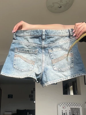 Blå jeansshorts - Blå denimshorts med klassisk femficksdesign. Shortsen har en ljus tvätt och råa benslut för en avslappnad look. Perfekta för varma dagar och enkla att matcha med olika toppar⛱️Kolla in min profil för fler fina och trendiga plagg!