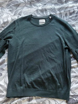 Mörkgrön tröja från GANT - Snygg mörkgrön tröja från GANT med rund halsringning och diskret logga på bröstet. Tröjan har långa ärmar och ribbade muddar vid ärmslut och nederkant. Perfekt för dig som gillar stilrena och klassiska plagg. Priset kan diskuteras!