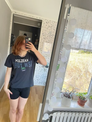 Svart Harlem New York t-shirt - Säljer en svart t-shirt med trycket 'HARLEM NEW YORK 1982' i vitt och grönt framtill. T-shirten har korta ärmar och en loose passform. Materialet känns som bomull. 