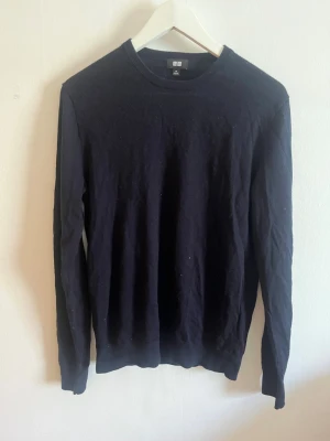 Mörkblå stickad tröja från Uniqlo - En stilren mörkblå långärmad tröja från Uniqlo med rund halsringning. Tröjan är enkel och passar perfekt till lager-på-lager. 100% wool