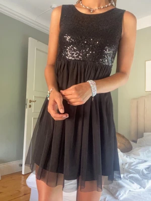 Svart paljettklänning med tyllkjol - ❣️gammal bildtagning❣️Supersnygg svart kortklänning med paljetter upptill och luftig tyllkjol. Ärmlös modell med rund halsringning, perfekt för att sticka ut. Klänningen har en glittrig överdel och ett flowy fall. Såååå fin när man är brun