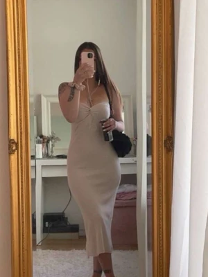 Beige ribbad långklänning omlott -  beige långklänning med ribbad struktur och omlottdetalj vid bysten. Klänningen är ärmlös och har en figurnära passform som framhäver siluetten.  Storlek S 