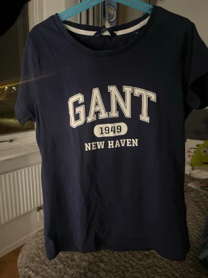Marinblå GANT t-shirt med tryck - Snygg marinblå t-shirt från GANT med klassiskt tryck framtill där det står 'GANT 1949 NEW HAVEN'. T-shirten har rund halsringning och korta ärmar. Perfekt för en avslappnad och sportig stil.