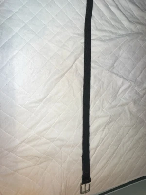 Svart flätat bälte med silverfärgat spänne - Snyggt svart flätat bälte med ett stilrent silverfärgat spänne. Perfekt accessoar för att lyfta din outfit och passar till de flesta byxor. Bältet är gjort i ett mjukt och flexibelt material som gör det bekvämt att bära hela dagen.