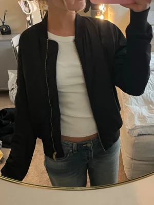 Svart bomberjacka med gulddragkedja - Snygg svart bomberjacka med guldfärgad dragkedja i storlek 38