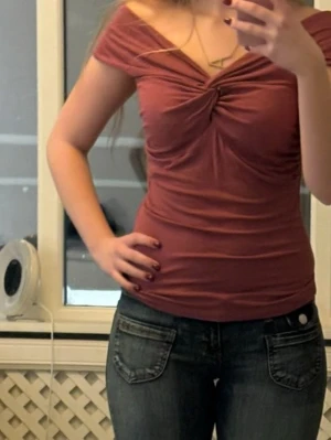 Rosa omlott topp med offshoulder - Trendig rosa topp med omlott-detalj och offshoulder-design. Snygg twist framtill och figurnära passform som framhäver siluetten. Perfekt för dig som gillar en feminin och modern stil.