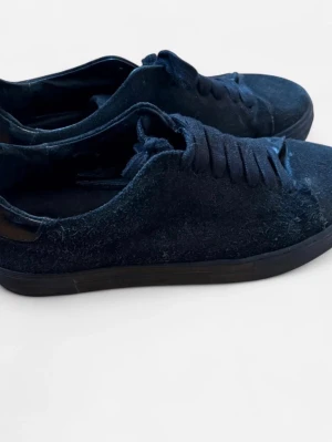 Mörkblå mockasneakers Jim Rickey - Stilrena mörkblå sneakers från Jim Rickey med ovandel i mocka och blanka läderdetaljer vid hälen. Klassisk låg modell med matchande mörkblå snören och svart sula. Perfekta för dig som gillar minimalistisk och trendig stil.