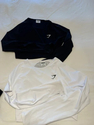 Långärmade cropade toppar från Gymshark - Två långärmade toppar från Gymshark, en i svart och en i vitt. Tumm topp.