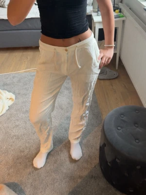 Beiga linnebyxor  - Snygga beiga linnebyxor med avslappnad passform och dragsko i midjan. Byxorna har knappgylf, sidofickor och en bakficka med knapp. Perfekta för en chill och stilren look. Tillverkade i luftigt linnematerial.
