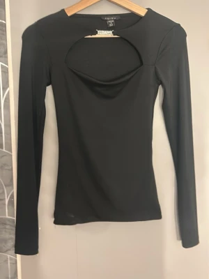Svart långärmad topp med cut out - Trendig svart långärmad topp från New York med en snygg cut out-detalj vid halsen. Figurnära passform och rund halsringning. Perfekt för dig som vill ha en stilren men edgy look. Liten S skulle säga att den passar en xs💕