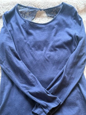 Mörkblå långärmad topp med spets - Mörkblå långärmad topp med rund halsringning och snygg spetsdetalj i ryggen. Tröjan är tillverkad i mjukt material som känns skönt mot huden. Perfekt att styla med jeans eller kjol.