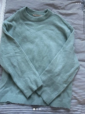 Ljusgrön stickad tröja - Mysig ljusgrön stickad tröja med rund halsringning och ribbade muddar vid ärmslut och nederkant. Perfekt för kyliga dagar och enkel att matcha med jeans eller kjol. Tröjan har en avslappnad passform och är tillverkad i mjukt material.