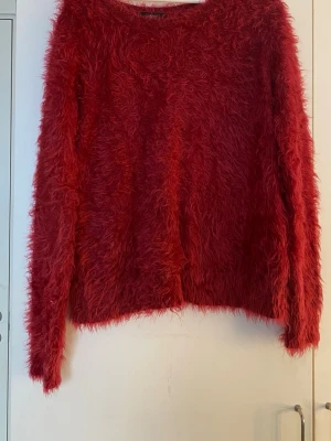 Röd fluffig stickad tröja Ellos - Säljer en röd, superfluffig stickad tröja från Ellos. Tröjan har lång ärm och är gjord i ett lurvigt material som ger en mysig och trendig look. Perfekt för dig som vill ha något extra mjukt och coolt i garderoben.