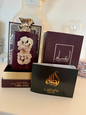 Lattafa Pride Ansaam Eau de Parfum - Lattafa Pride Ansaam Eau de Parfum i en lyxig mörkröd flaska med guldfärgade blommönster och elegant guldkork. Flaskan rymmer 100 ml och kommer i en matchande dekorativ ask. Perfekt för dig som gillar exklusiva och unika dofter.jag har endast testat det två-tre sprut