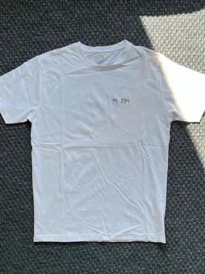 Handbroderad vit t-shirt från Denim Project - Vit t-shirt från Denim Project med broderad text 'PS 23:4' på bröstet. "Även om jag vandrar genom dödsskuggans dal fruktar jag inget ont, ty du är med mig. Din käpp och din stav, de tröstar mig."