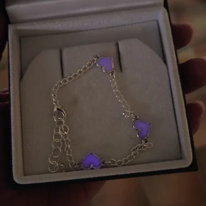 Silverarmband med självlysande hjärtan - Snyggt armband i silverfärgad rostfritt stål med tre vita hjärtan som lyser lila i mörkret. Hjärtana är jämnt placerade längs kedjan och ger en unik touch till din stil. Perfekt för dig som gillar detaljer som sticker ut och vill ha något annorlunda. Vanligt dagsljus och solljus aktiverar ljus-effekten och håller i många timmar vid normal användning. Handgjort. Både kedjan & hängena tål vatten och missfärgas inte.