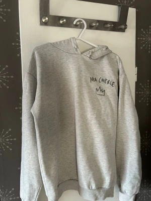 Grå hoodie med tryck 'MA CHÉRIE' - Den är lite knopprig och saknar en av metall grejerna på snöret