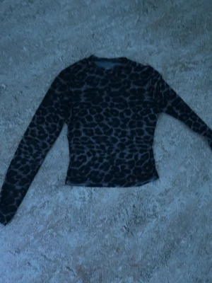Leopardmönstrad mesh topp - Snygg långärmad topp i mesh med leopardmönster i svart och grått. Tight passform och transparent material som ger en edgy vibe. Perfekt att styla lager på lager eller som statement piece.