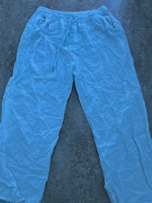 Vita linnebyxor - Säljer ett par vita linnebyxor med avslappnad passform och resår i midjan. Byxorna har raka ben och sidofickor. Perfekta för en chill och luftig stil under varma dagar.