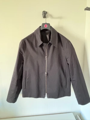 Tiger Of Sweden Barnaby C Zip Shirt Jacket - Stilren svart jacka med rak passform och klassisk krage. Jackan har en enkel design med dragkedja framtill och är tillverkad i ett slätt material. Dragkedjan går åt båda hållen. Perfekt för dig som gillar en clean och modern look. Nypris 2499kr