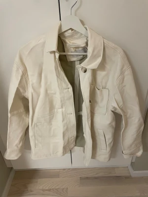 Vit bomberjacka i bomull - Snygg vit bomberjacka med klassisk krage och dragkedja framtill. Jackan har två sidofickor och en bröstficka.