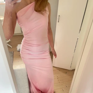 Ljusrosa oneshoulder långklänning - Säljer en elegant ljusrosa långklänning med oneshoulder-design. Klänningen har figurnära passform och fina draperingar längs sidorna som ger en snygg siluett. Perfekt som balklänning! Är från by ice, men köpt från Sellpy. Helt oanvänd med prislapp på