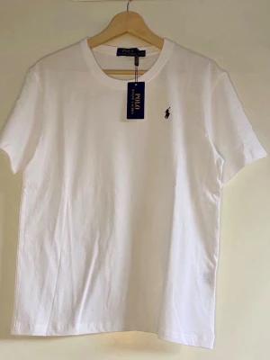 Vit t-shirt från Polo Ralph Lauren - Klassisk vit t-shirt från Polo Ralph Lauren i mjuk bomull. T-shirten har rund halsringning och korta ärmar, perfekt för en clean och enkel stil. Passar till allt och är ett måste i garderoben.