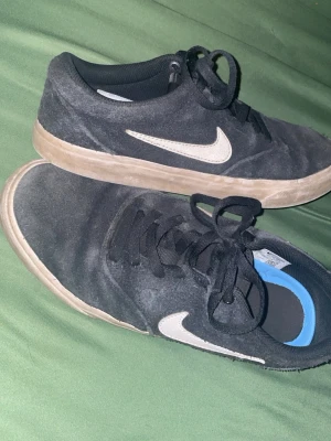 Svarta Nike sneakers med vit sula - Svarta sneakers från Nike med vit swoosh-logga på sidan och vit/beige sula. Skorna har lågt skaft, svarta skosnören och ovandel i mockaliknande material. Perfekta för en avslappnad streetstil. (Köpt för 659kr) 