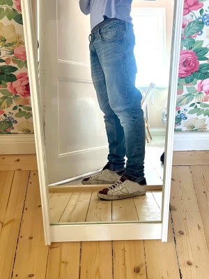 Blå slim fit jeans - Säljer ett par blå slim fit jeans med klassisk femficksdesign och dragkedja. Jeansen har en snygg ljusblå tvätt och är tillverkade i denim med stretch för extra komfort. Perfekt för dig som gillar en modern och stilren look.
