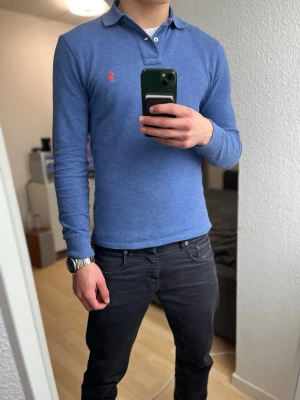 Ralph Lauren piké långärmad   - Säljer en blå långärmad pikétröja från Ralph Lauren med klassisk krage och två knappar. Tröjan har den röda broderade loggan på bröstet och är gjord i mjukt bomullstyg. Perfekt för dig som gillar stilrena och tidlösa plagg. Storlek S! Skriv om ni har några funderingar☺️
