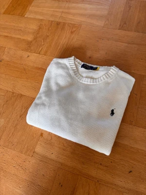 Vit stickad tröja från Polo Ralph Lauren - Klassisk vit stickad tröja från Polo Ralph Lauren med rund halsringning och den ikoniska mörkblå broderade loggan på bröstet. Mycket bra skick och storlek S. Perfekt till en kalla sommarkväll.Hör av er vid intresse!!