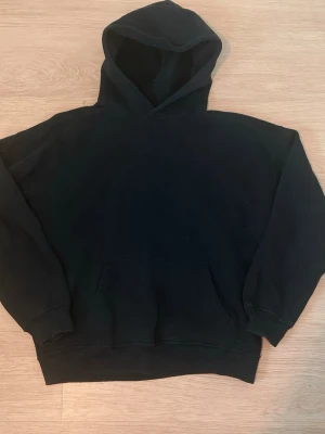 Svart hoodie från Abercrombie & Fitch - Klassisk svart hoodie från Abercrombie & Fitch med stor huva och magficka. Tillverkad i mjukt bomullsmaterial som känns skönt mot huden. Perfekt för en avslappnad och stilren look. Ribbade muddar vid ärmslut och nederkant.