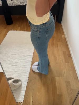 Ljusblå bootcut jeans - Säljer ett par ljusblå bootcut jeans med klassisk femficksdesign och normal midja. Jeansen har en snygg tvätt och är tillverkade i ett mjukt denimtyg med lite stretch för extra komfort. Perfekta till sneakers eller boots. 