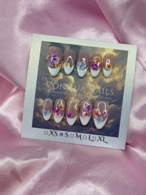 Flora (S);Medium Almond - Handgjorda press-on naglar i en medium lång almondform. Naglarna har en nude bas med handmålad vit fransk tipp och dekoreras med vackra blommor i lila, rosa, blått och gult. Perfekt för dig som vill ha en unik och kreativ nageldesign.S: 15 mm, 11,5 mm, 12 mm, 11 mm, 9 mm 