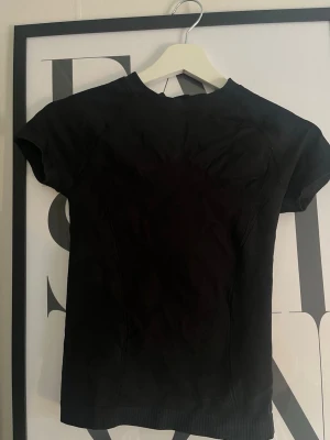 Svart tight tränings t-shirt - En enkel svart t-shirt med tight passform och korta ärmar. T-shirten har rund halsringning och är tillverkad i ett stretchigt material som sitter snyggt på kroppen. Perfekt basplagg till garderoben.
