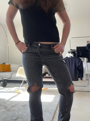 Svarta slitna jeans med hål - Säljer dessa svarta lågmidjade jeans med slitningar och hål på knäna. Storleken är 164 (passar typ xxs-xs) jeansen har en slits där nere. Bootcut modell!