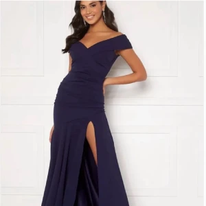 Marinblå långklänning med slits - Säljer en marinblå långklänning med offshoulder och snygg v-ringning. Klänningen har en hög slits på ena sidan och draperad överdel som ger en elegant siluett. Perfekt för bal eller student! Storlek är UK 12 EUR 42 US 10 men jag skulle säga att den är syl EUR 40-42 men de är ganska mycket stretch i klänningen så den är väldigt bekväm