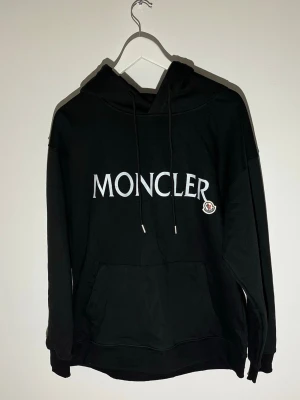 Moncler Hoodie - Säljer en Moncler Hoodie med ett tryck på bröstet samt en moncler logga vid sidan av trycket. Tröjans pris är som det är eftersom Moncler Loggan är dåligt sydd. Tröjan Är storlek L och passar en person som är 180-185