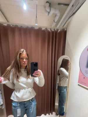 Vit omlottopp med knyt i midjan - Trendig vit omlottopp med knytband i midjan och lång ärm. Toppen har en lätt volang nedtill och är tillverkad i ett mjukt material som ger en snygg siluett. Perfekt att styla med jeans eller kjol för en fräsch look.