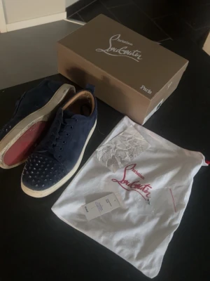 Christian Louboutin - Snygga mörkblå sneakers från Christian Louboutin i mocka med ikoniska nitar på tån och klassisk röd sula. Skorna har vita sulor och levereras med originalkartong och dustbag kvitto följer även med.  (Skorna har tappar några nitar) 2 extra nitar medföljer! 